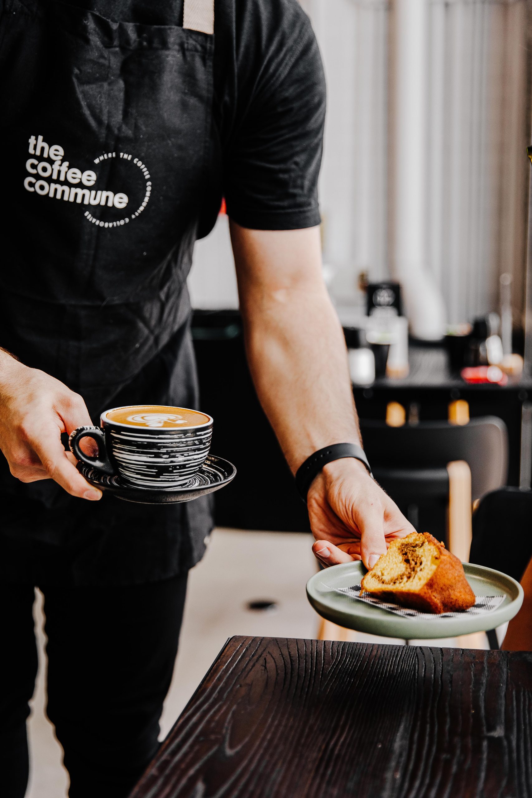 Man in Coffee Commune Uniform serving a coffee and cake